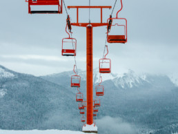 A bright red chairlift at the Manning Park Ski Resort in British Columbia. In the background, snow is falling on the surrounding mountains.