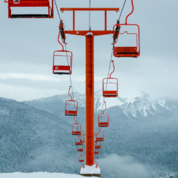 A bright red chairlift at the Manning Park Ski Resort in British Columbia. In the background, snow is falling on the surrounding mountains.