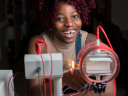 A young female engineering student smiles and laughs while she uses a piece of electrical engineering test equipment.