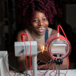 A young female engineering student smiles and laughs while she uses a piece of electrical engineering test equipment.
