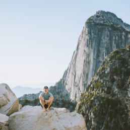 Photographer Alex Mey is seen here resting at the top of a hike. Mountains from the Cascade Range are visible in the background.