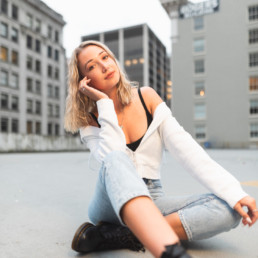 A young woman strikes a casual pose at a photoshoot location in downtown Vancouver. Old buildings surround the location with their architectural details visible.