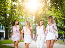 Four women walk along a pathway on the campus of University of British Columbia, located in Vancouver, BC. The spring sunshine shines through the foliage, casting a golden glow on the women.