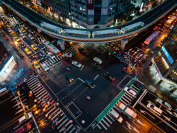 A photo taken from a Taipei rooftop looking down at a busy intersection. A Taipei MRT train and many colourful umbrellas of pedestrians crossing the intersection are visible.