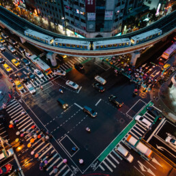 A photo taken from a Taipei rooftop looking down at a busy intersection. A Taipei MRT train and many colourful umbrellas of pedestrians crossing the intersection are visible.